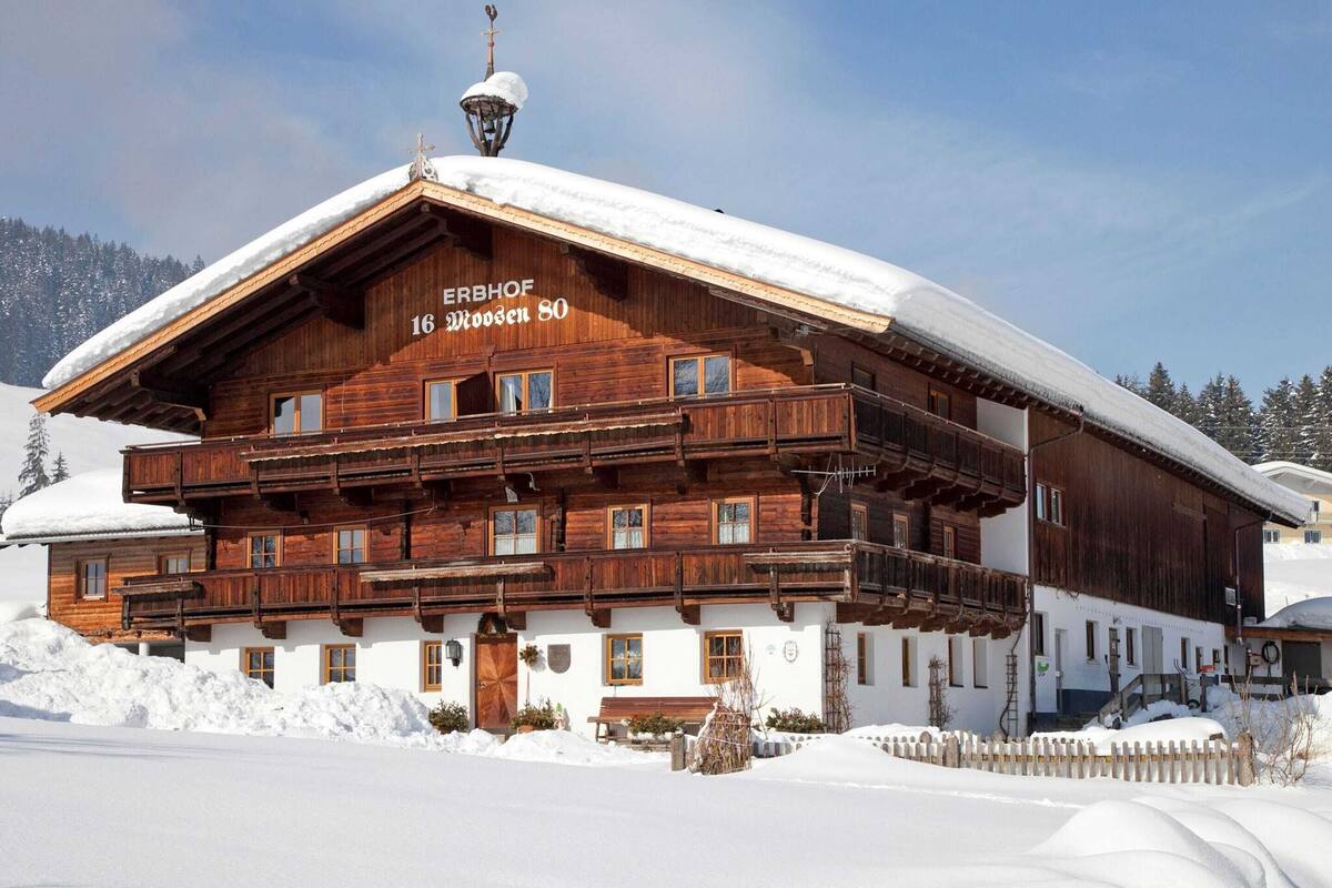 A wooden chalet named ERBHOF 16 MOOSEN 80 with a snow-covered roof and a balcony.