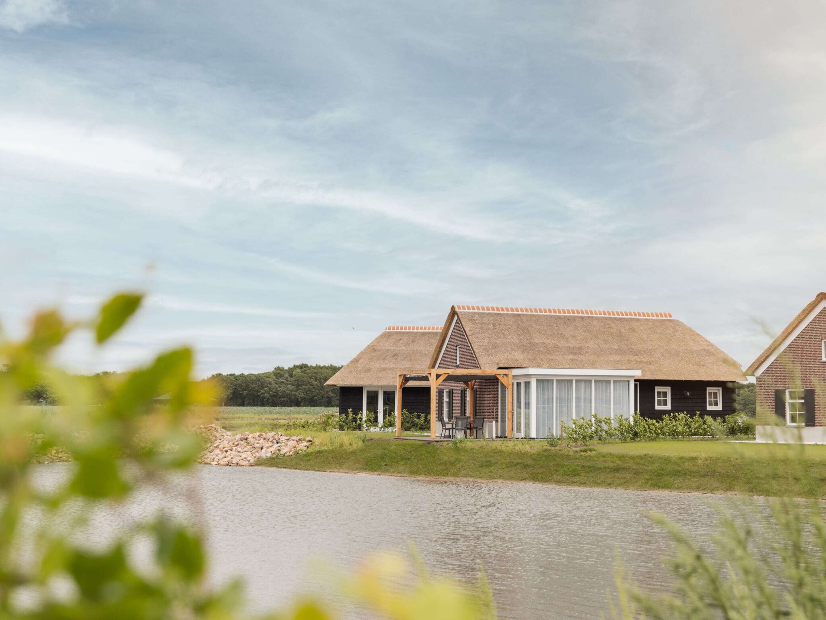 A row of traditional-style houses with thatched roofs, situated beside a calm body of water, likely a lake or pond.