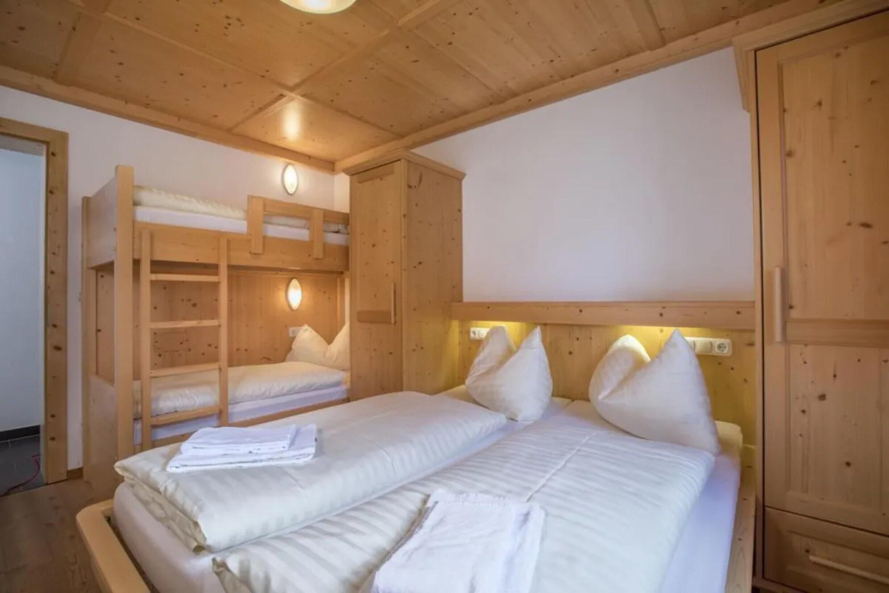 A wooden room with bunk beds, a flat bed with pillows, and a wooden wardrobe.