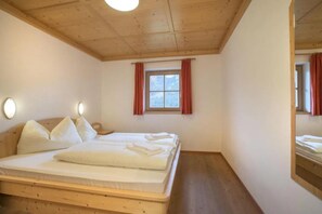 A bedroom with a wooden ceiling, a bed with white bedding, a window with red curtains, and a mirror on the wall.