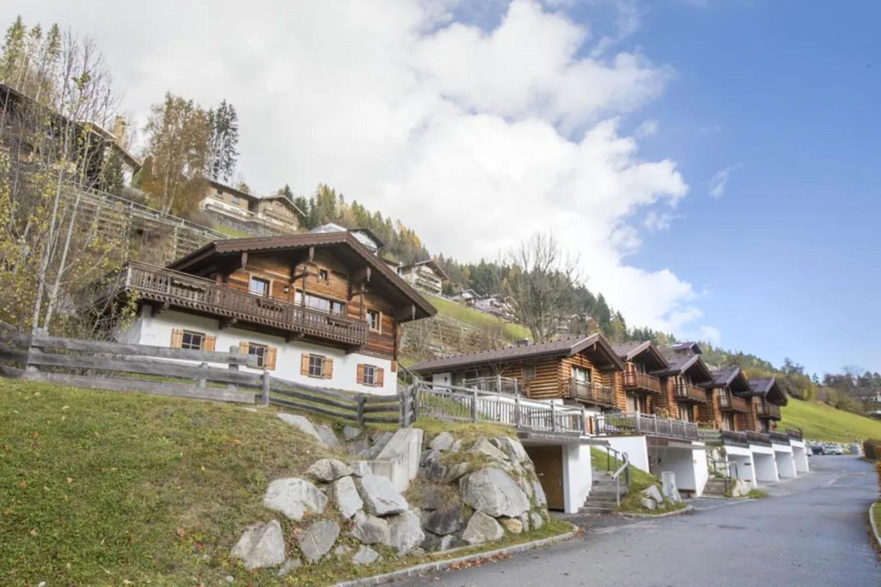 Una hilera de tradicionales chalets de madera con balcones, con un fondo de árboles y cielo despejado.