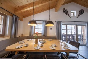 A dining area with a large wooden table set for four, two pendant lights, and a view of the outdoors through large windows. - Restful Chalet in Wald-Königsleiten near Ski Bus (Wald im Pinzgau)