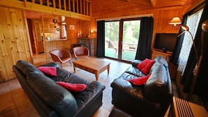 A wooden cabin interior with a living area featuring two black leather sofas, a wooden coffee table, and a fireplace. - Chalet in Beffe With Hot Tub & Valley Views (Rendeux)