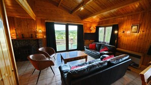 A cozy wooden interior with a fireplace, leather sofa, and a view through the glass doors. - Chalet in Beffe With Hot Tub & Valley Views (Rendeux)