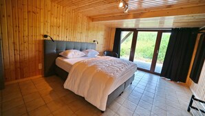 A bedroom with a bed, wooden walls, a window, and a door. - Chalet in Beffe With Hot Tub & Valley Views (Rendeux)