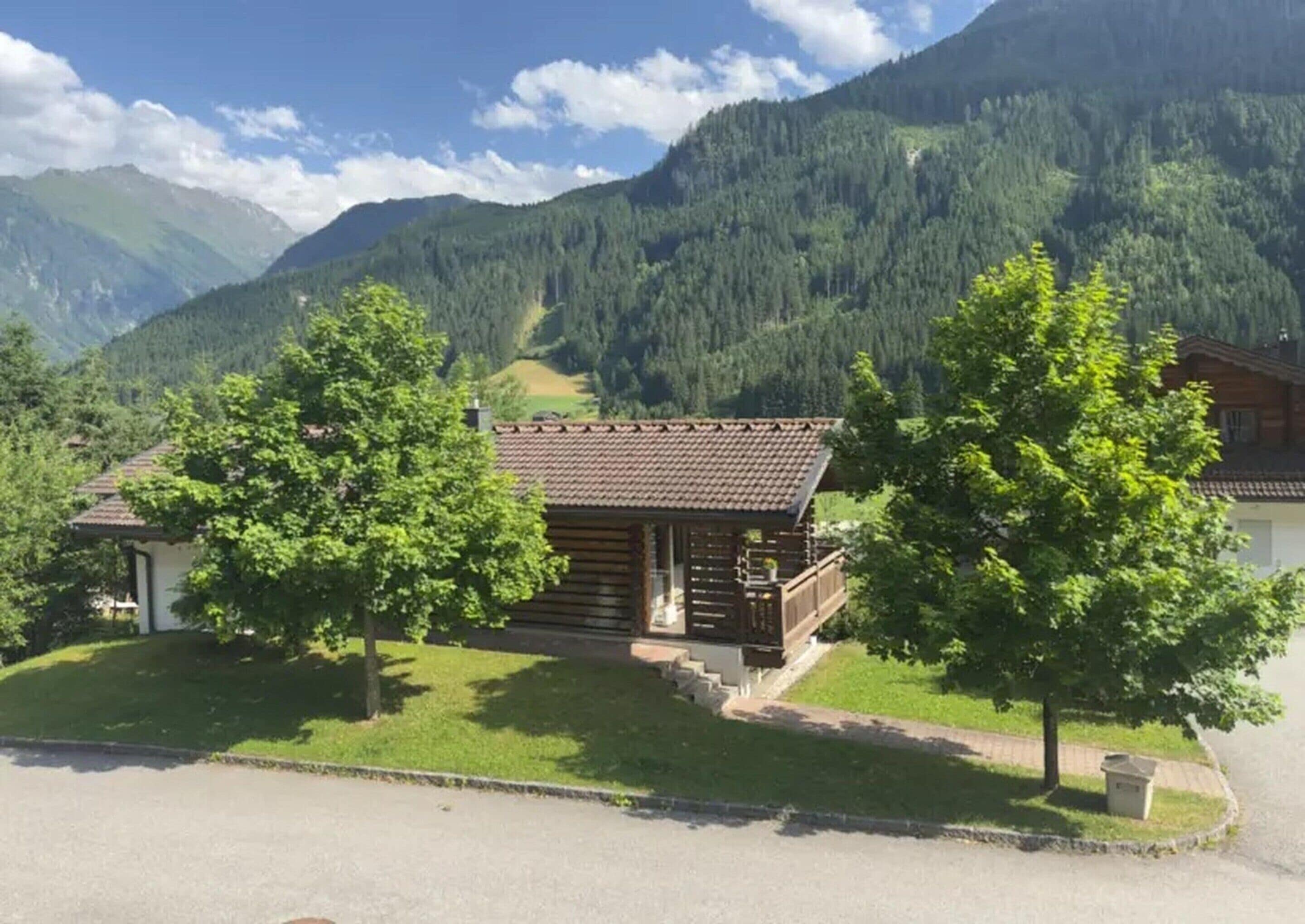 Eine Holzhütte mit einem Balkon, umgeben von üppiger Vegetation und Bergen im Hintergrund.
