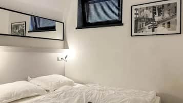 Quarto com uma cama de solteiro, janela com persianas, luminária na parede e um quadro emoldurado.