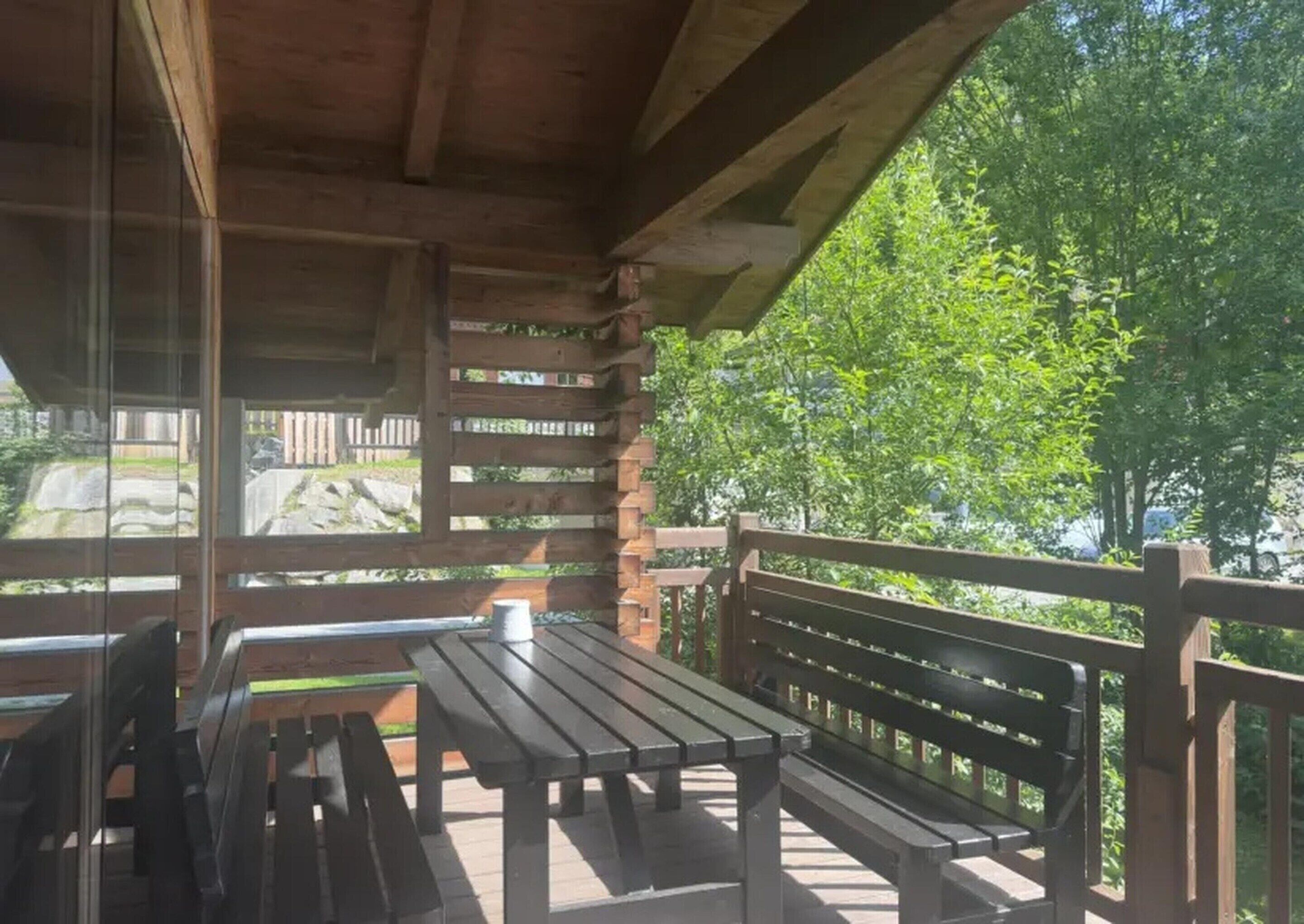 Um deck de madeira ao ar livre com bancos e uma mesa, com vista para uma paisagem natural.