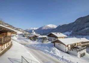 A snow-covered village with traditional wooden houses, a church, and mountains in the background. - Chalet Retreat With Sauna in Wald (Wald im Pinzgau)
