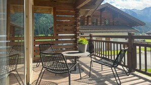 A wooden balcony with a table and chairs, overlooking a mountainous landscape.