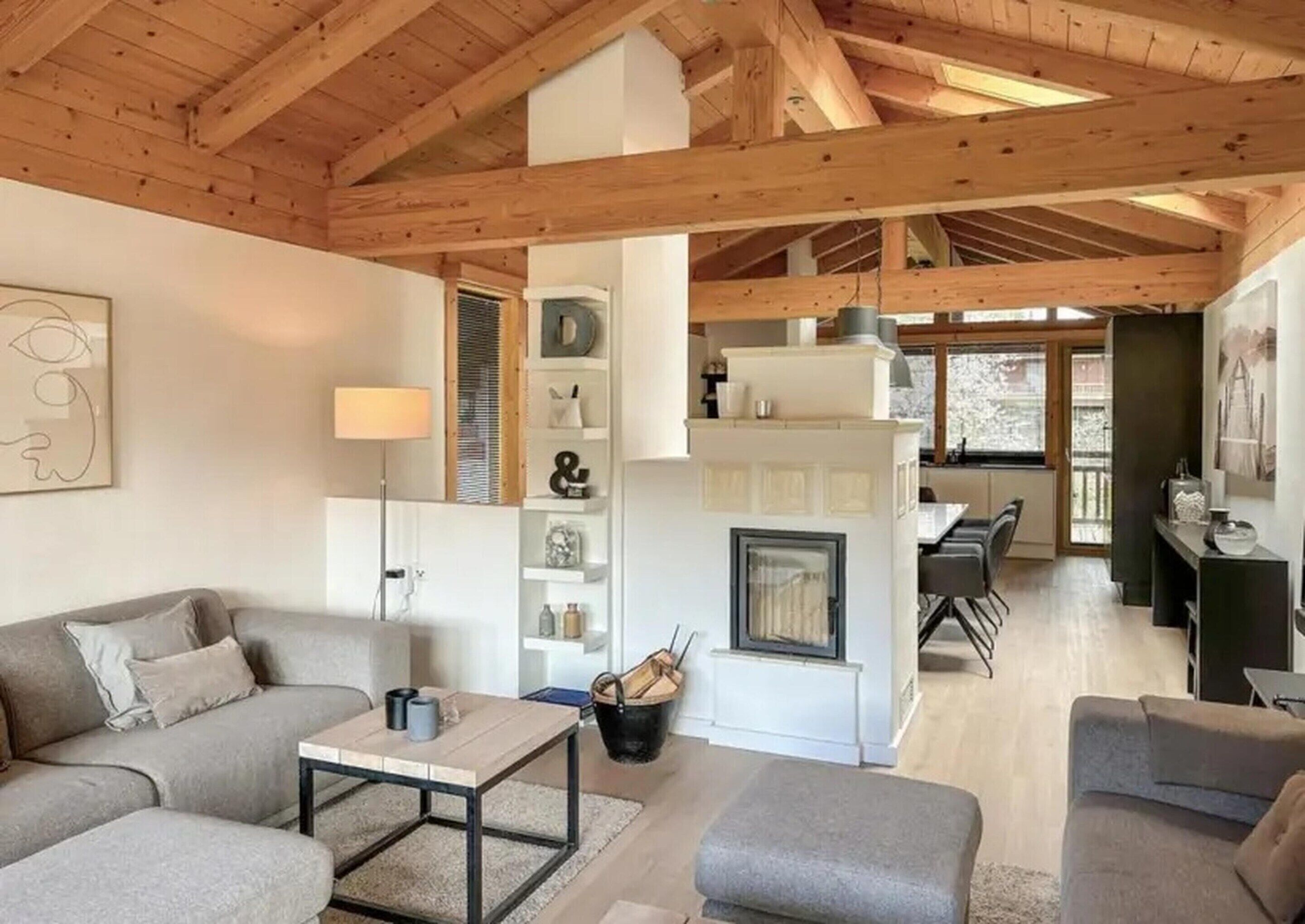 A spacious living area with a high ceiling, wooden beams, a fireplace, and a dining area with a view.