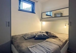 A single bed with a gray mattress and pillows, a small window with blinds, and a mirror above the bed. - Chalet Retreat With Sauna in Wald (Wald im Pinzgau)