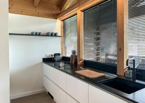 A modern kitchen with a black countertop, a wooden cutting board, and a built-in sink. - Chalet Retreat With Sauna in Wald (Wald im Pinzgau)