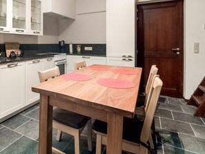 Een keuken met een houten tafel, vier stoelen en een donkere betegelde vloer.