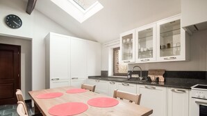 Una cocina moderna con armarios blancos, una mesa de comedor de madera con individuales rosas, y un tragaluz arriba.