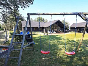 A wooden swing set in a backyard with a house in the background. - Holiday Home in Løkken (Lokken)
