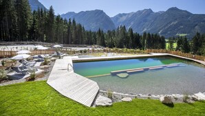 Une piscine avec une terrasse en bois, entourée d’une forêt et de montagnes.