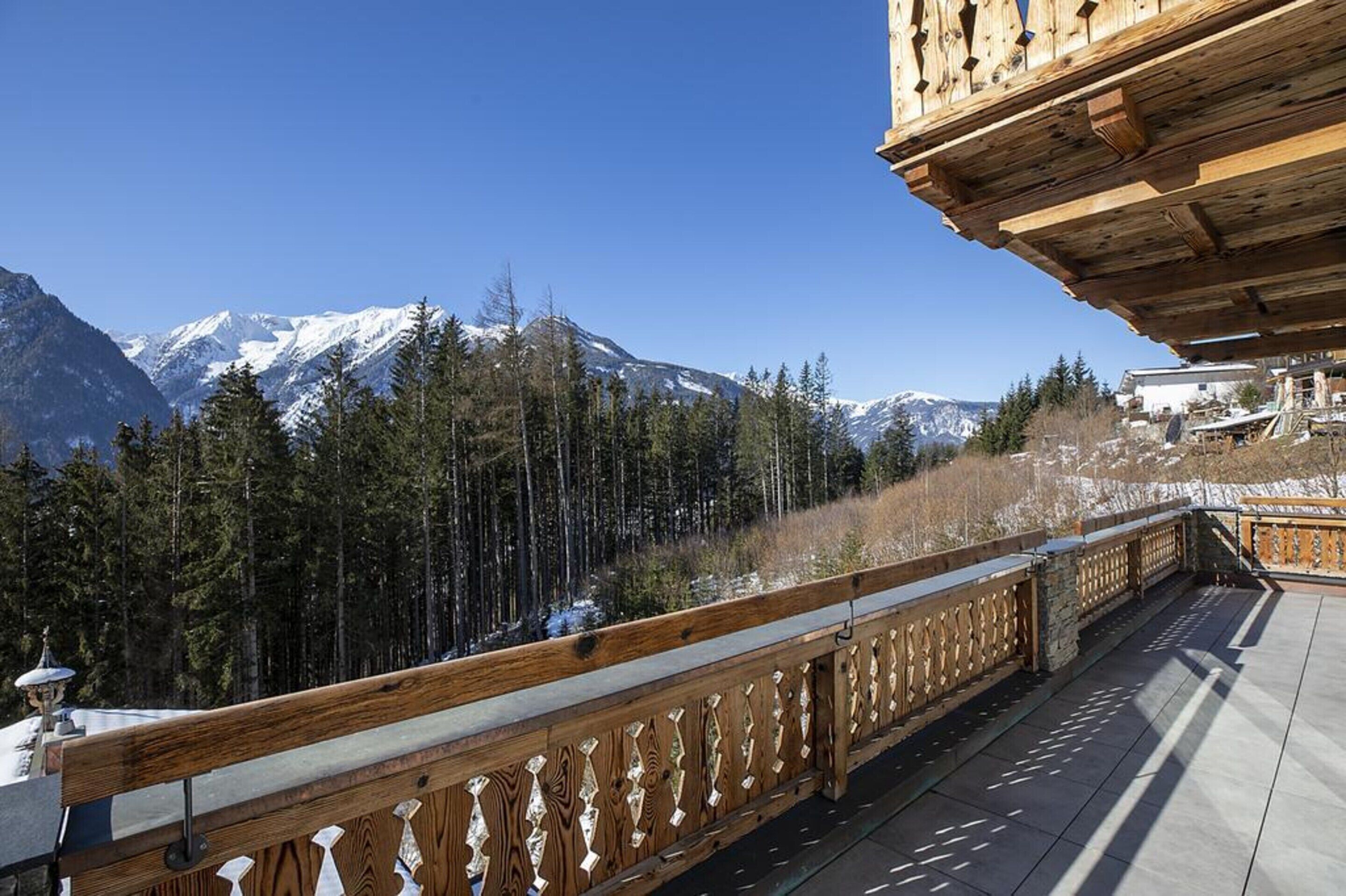 A wooden balcony with a view of snow-capped mountains and pine trees.