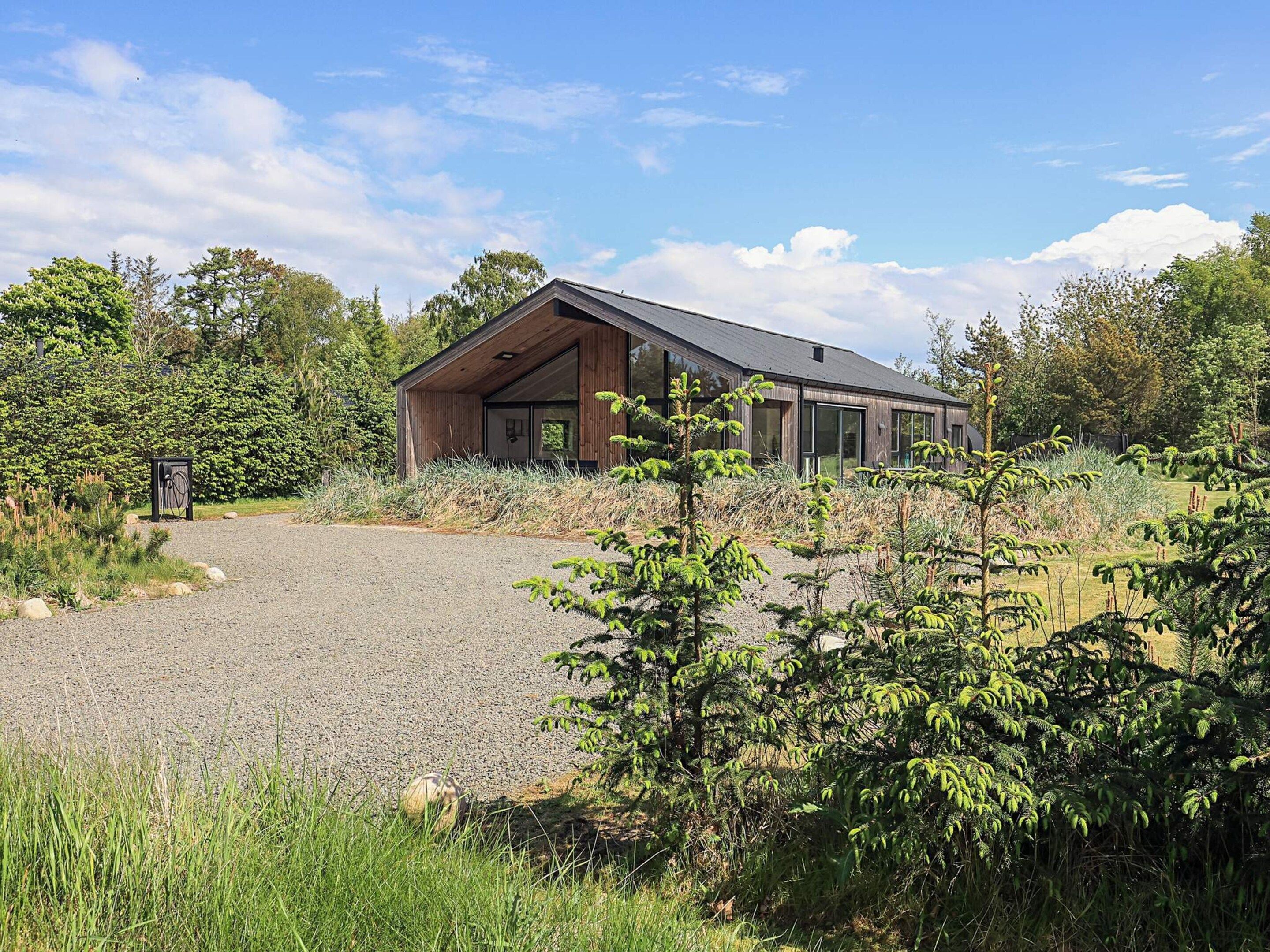 A modern building with a sloped roof, large windows, and a gravel driveway leading to it.