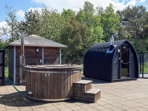 A wooden hot tub with steps, a small wooden building, and a covered structure with a chimney.