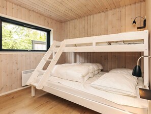 A bunk bed with a ladder, a window with a view of greenery, and a wall-mounted lamp.