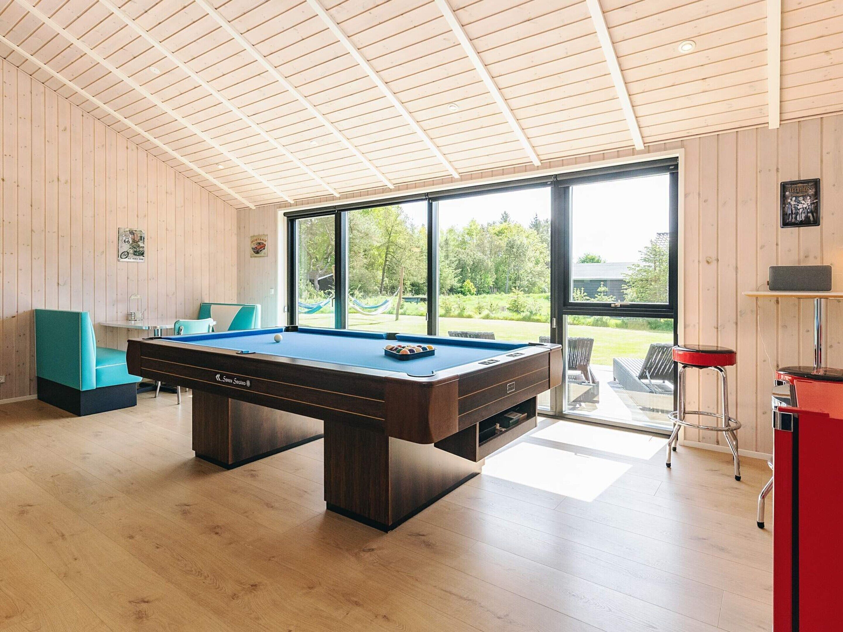 A pool table in a room with wooden walls and large windows.