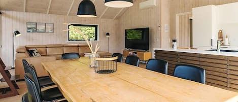 A modern interior with a wooden dining table, black chairs, a sofa, and a TV.