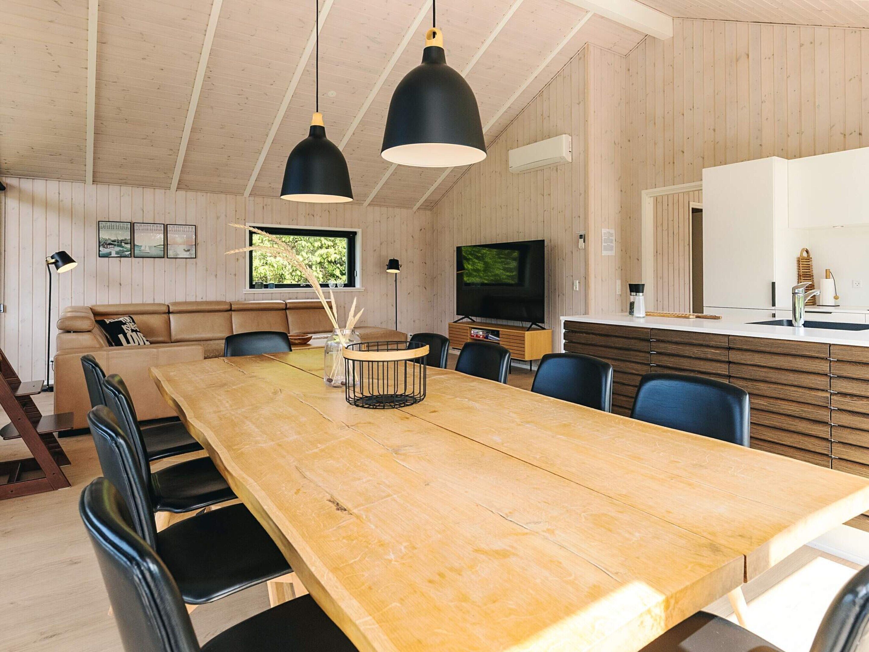 Un intérieur moderne avec une table à manger en bois, des chaises noires, un canapé et un téléviseur.