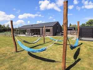 Een modern huis met een ruim terras, een hangmat en een houten omheining.