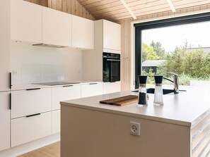 Een moderne keuken met witte kasten, een zwarte oven en een raam met uitzicht op groen.