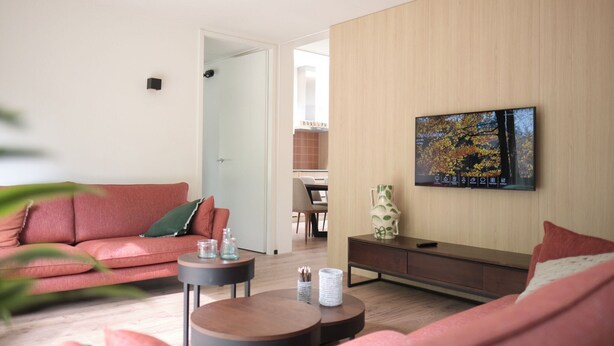 A modern living room with a sofa, coffee table, and a flat-screen TV mounted on the wall. - Detached Lodge Near Maastricht (Gulpen)