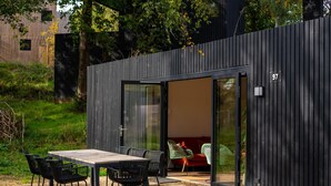 A modern outdoor dining area with a table and chairs, a sliding glass door leading to a seating area, and a number '97' on the building. - Detached Lodge Near Maastricht (Gulpen)