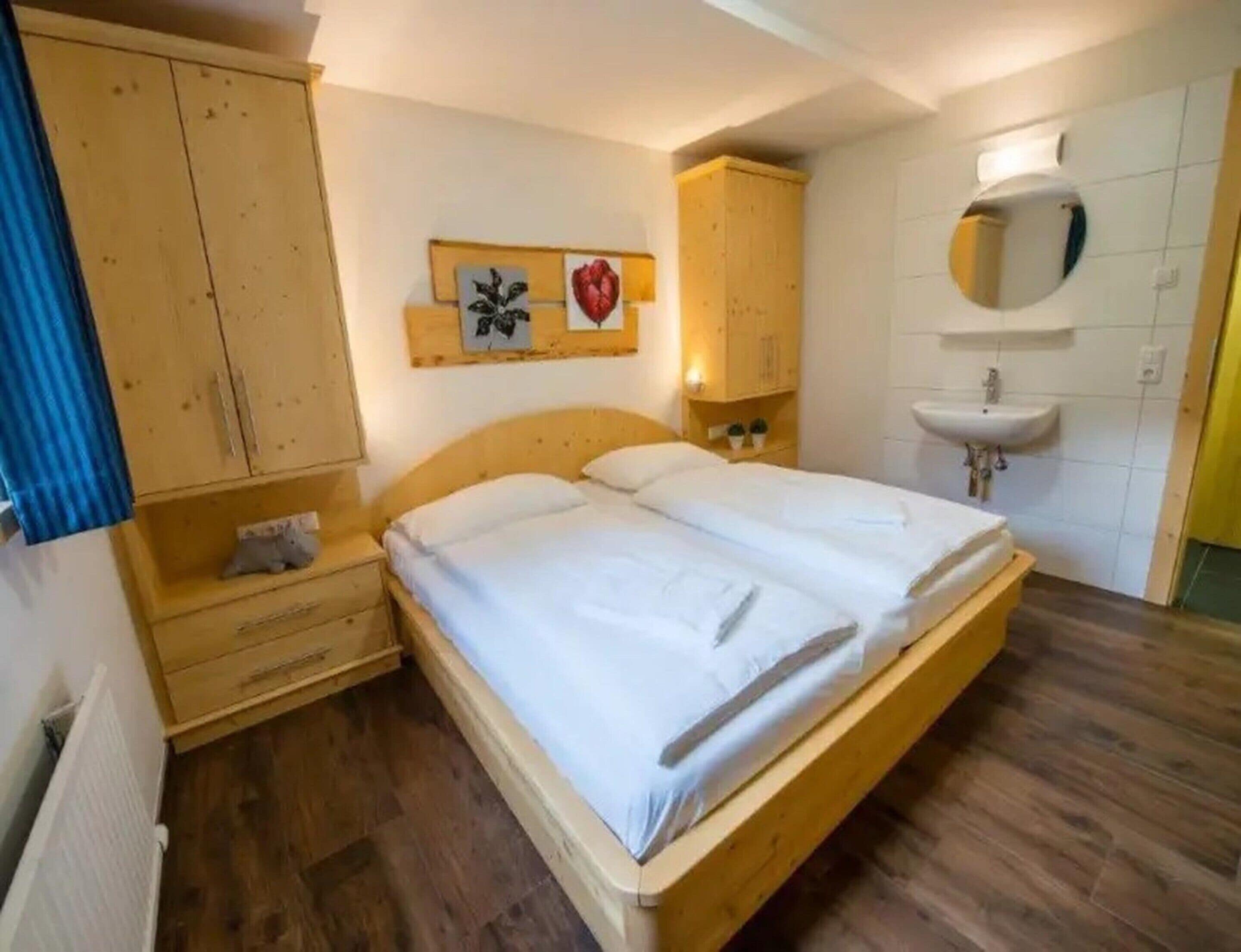 Un dormitorio con cama doble, armario de madera, mesita de noche y espejo instalado en la pared.