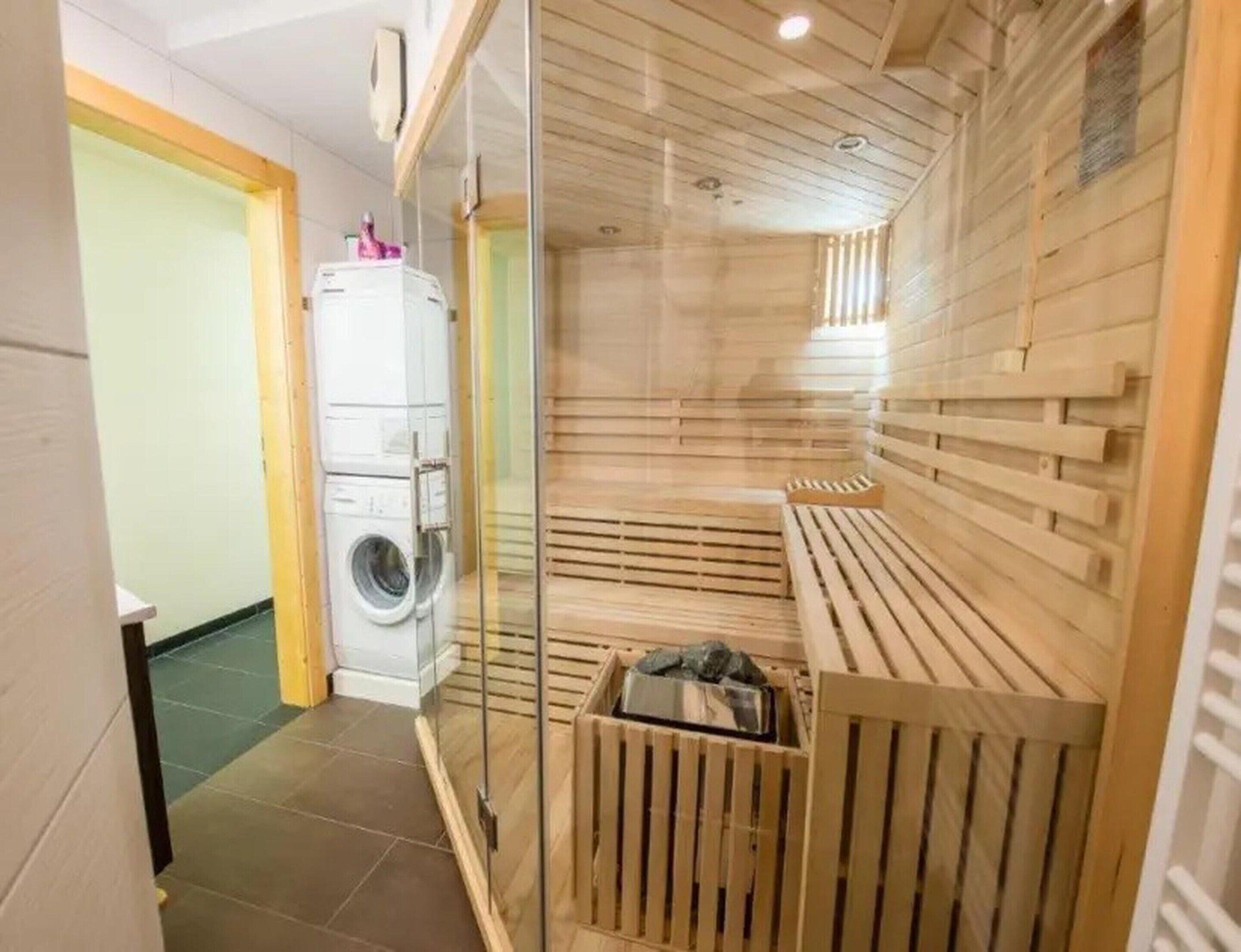 Uma sala de sauna com um banco de madeira, um painel de vidro e uma máquina de lavar no quarto vizinho.