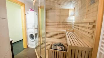Uma sala de sauna com um banco de madeira, um painel de vidro e uma máquina de lavar no quarto vizinho.