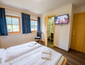 A hotel room with a bed, a chair, a television, and a door leading to a bathroom. - Cozy Chalet with 4 Bathrooms near Königsleiten (Wald im Pinzgau)