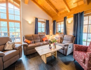 A cozy living room with a wooden ceiling, large windows with curtains, and a central coffee table. - Cozy Chalet with 4 Bathrooms near Königsleiten (Wald im Pinzgau)
