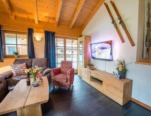 A living room with a sofa, armchair, coffee table, TV, wooden cabinet, and skis on the wall. - Cozy Chalet with 4 Bathrooms near Königsleiten (Wald im Pinzgau)