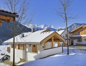 A chalet-style building with a sloped roof, wooden beams, and a view of snow-covered mountains.