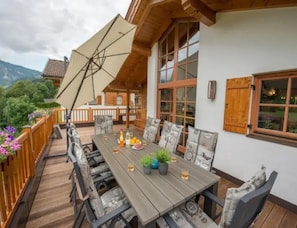 A wooden deck with a dining table and chairs, surrounded by a wooden railing and potted plants.