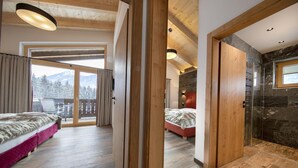 Une chambre à coucher avec un lit, un plancher en bois, une fenêtre et un balcon offrant une vue sur des montagnes enneigées.