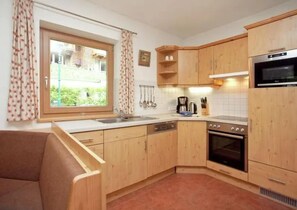 A compact kitchen with wooden cabinets, a built-in oven, and a window with curtains. - Snug Holiday Home in Wald-Königsleiten near Cross Country (Wald im Pinzgau)
