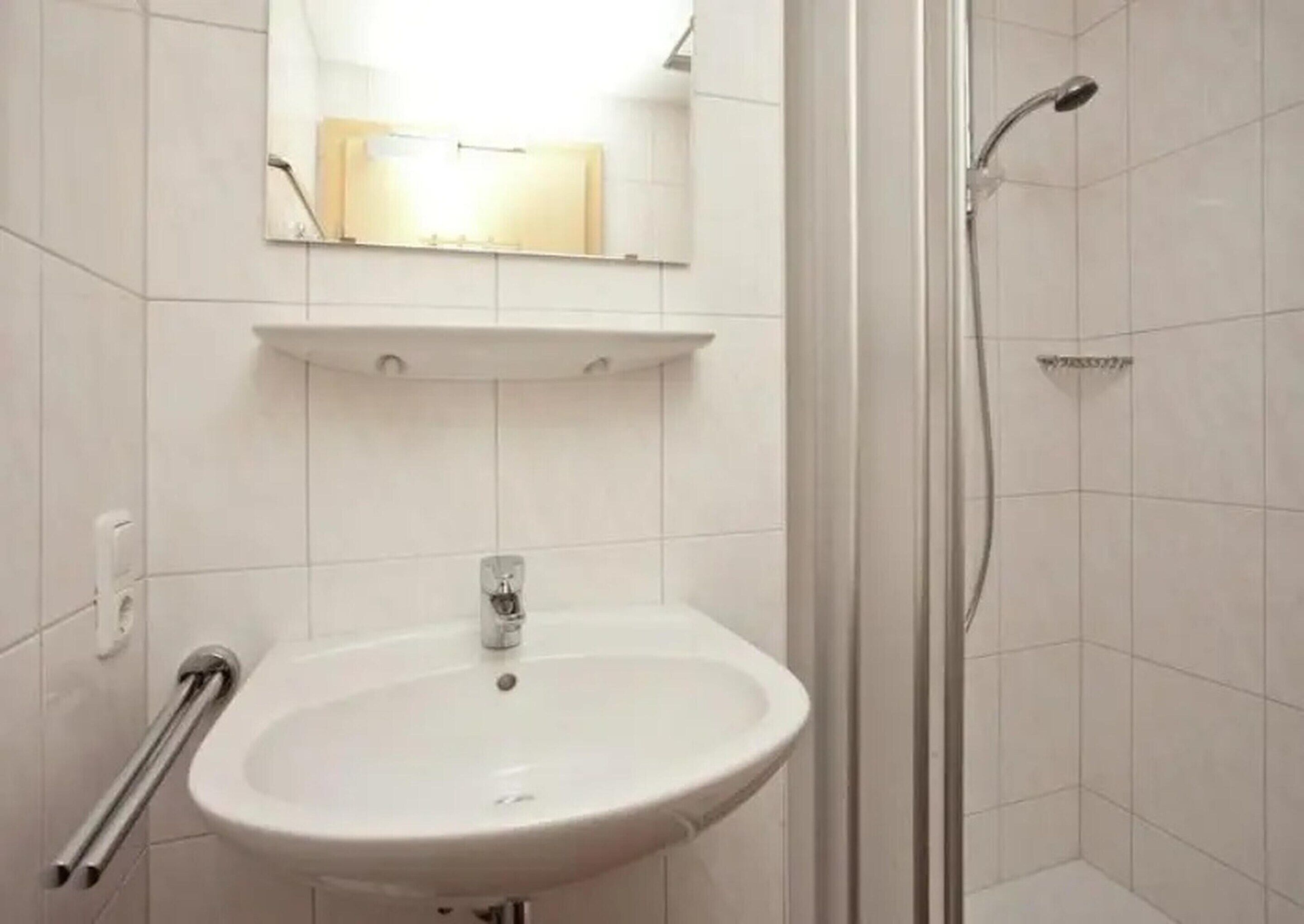 Un baño con lavamanos blanco, un espejo encima y zona de ducha.