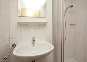 Un baño con lavamanos blanco, un espejo encima y zona de ducha.