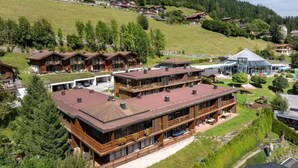 A multi-story hotel with a large balcony area, surrounded by lush greenery and a hilly landscape. - Snug Holiday Home in Wald-Königsleiten near Cross Country (Wald im Pinzgau)