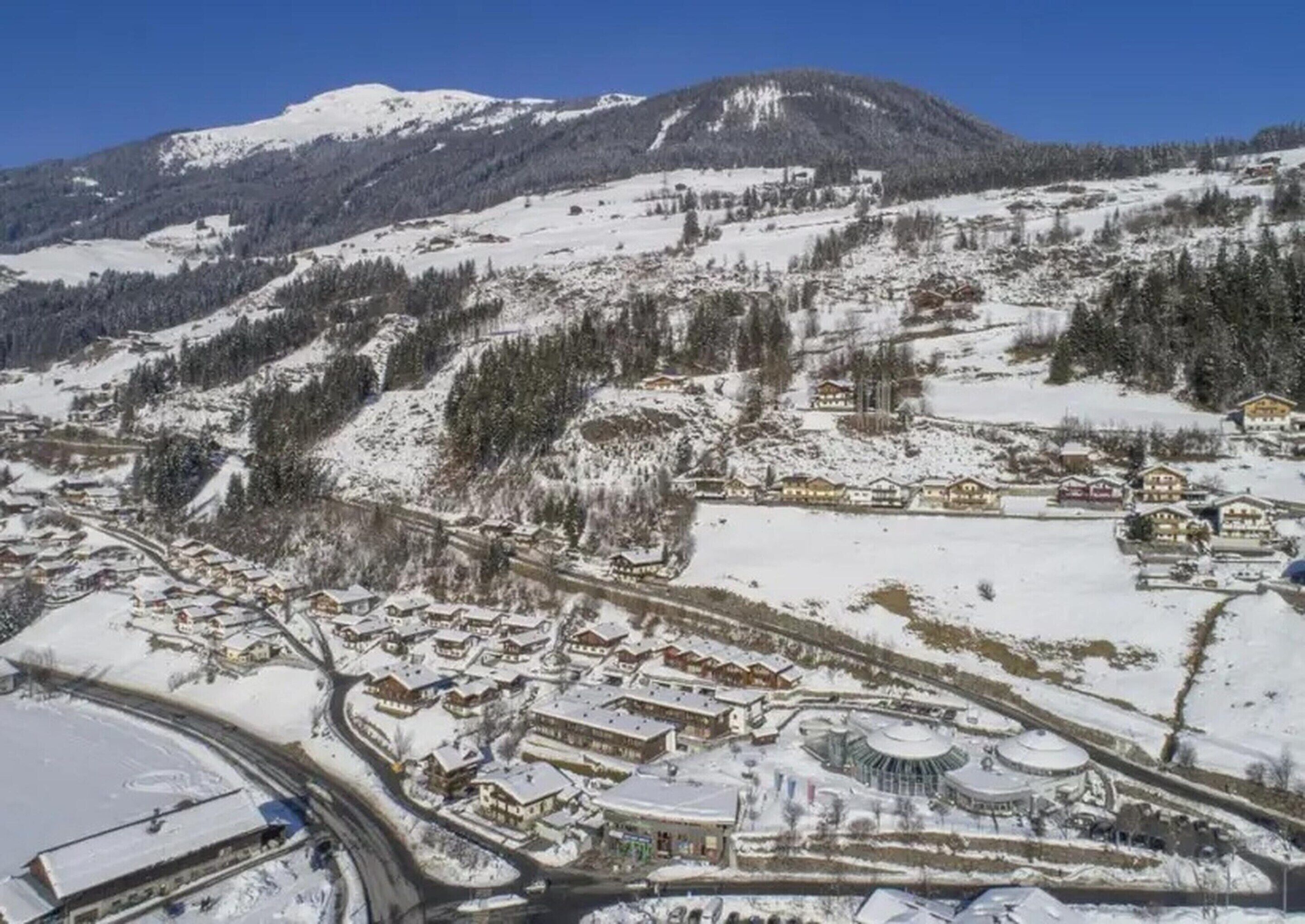 A snow-covered village with traditional buildings, a central round structure, and a mountain backdrop.