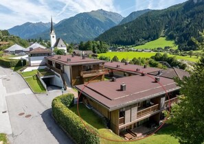 A two-story building with a red roof, a visible staircase, and a church in the background. - Snug Holiday Home in Wald-Königsleiten near Cross Country (Wald im Pinzgau)