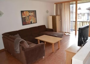 Een woonkamer met een bruine bank, een houten salontafel, een televisie en een schilderij aan de muur.