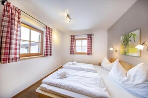 A hotel room with two beds, a window with curtains, a bedside table, and a wall-mounted lamp. - Cozy Chalet with Sauna near Königsleiten (Wald im Pinzgau)