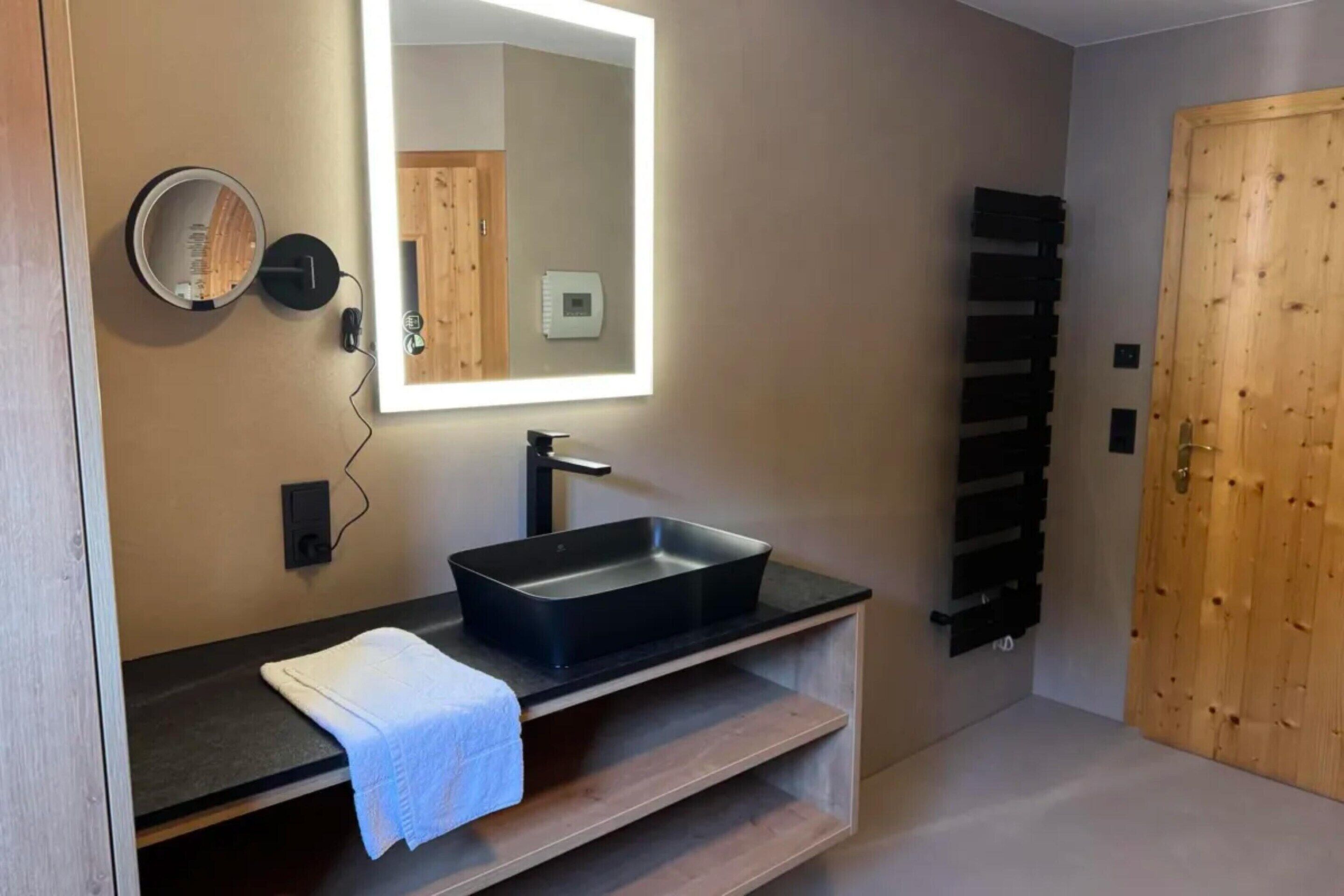 A modern bathroom with a black sink, a mirror, a towel, and a wooden door.